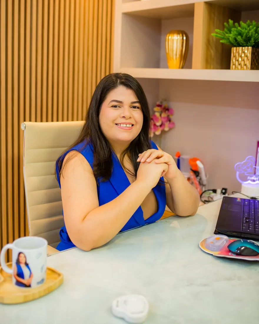 Dra. Hanna Emile sentada à mesa do consultório, de vestido azul